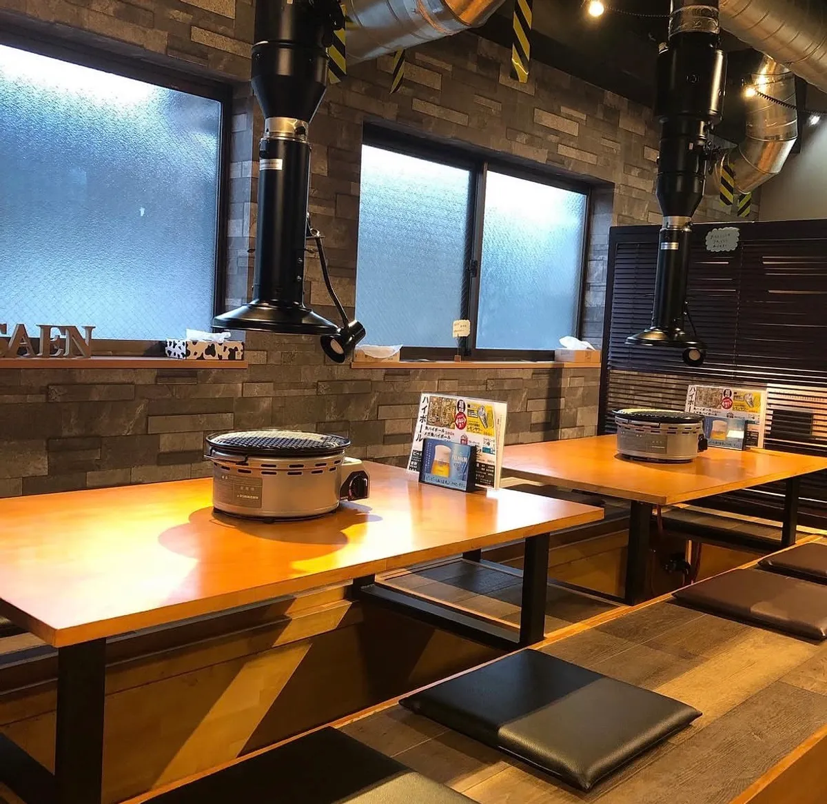 炭火ホルモン 煙の店内テーブル席 石壁とダクトのある落ち着いた空間
